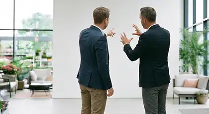 Two men stand with their backs to the camera in an office, gesturing as they discuss a concept. AI-generated image.