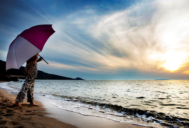 A woman stands under the Schneider Easy parasol, gazing at the sea during sunset.