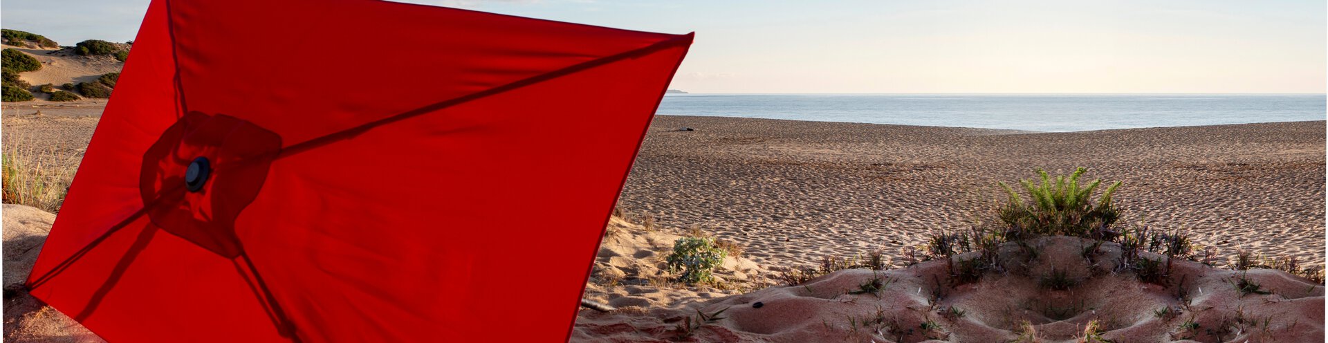 Der geöffnete Sonnenschirm Sevilla von Schneider liegt stimmungsvoll in den Dünen am Meer – modernes Design, höhenverstellbar, mit komfortablem Push-Up und UV-Schutz 50+ für Garten, Terrasse oder Balkon.