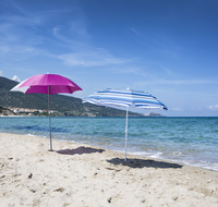 Two Schneider parasols on the beach: the Shorty model with blue and white striped fabric and the Easy model in pink and white – both offer flexible sun protection and are suitable for beach and open-air bath use.