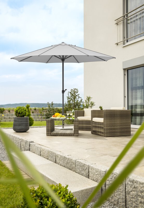 Schneider Sonnenschirm Adria in Silbergrau, 350 cm Durchmesser, auf einer Terasse, darunter Lounge-Möbel. Auf dem Tisch eine Obstschale, eine Flasche und Gläser. Im Hintergrund eine gestufte Stützmauer aus Betonsteinen. Um die Terrasse Wiese und Sträucher.
