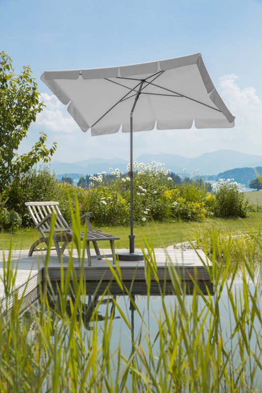 Schneider Aquila parasol in silver grey, 225x120 cm, on a wooden terrace by a natural swimming pool. A deck chair sits beneath it. Reeds are in the foreground and meadows and shrubs are in the background.