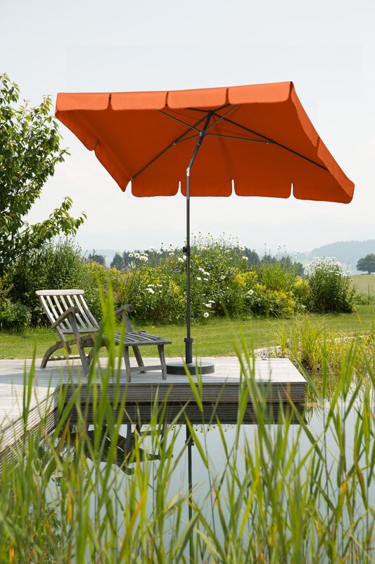 Schneider Aquila parasol in terracotta, 225x120 cm, on a wooden terrace by a natural swimming pool. A deck chair sits beneath it. Reeds are in the foreground and meadows and shrubs are in the background.