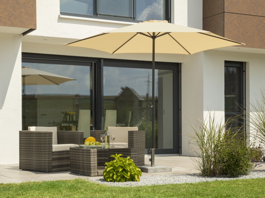 Schneider Sonnenschirm Bergamo in Natur, 300 cm Durchmesser, auf einer Terrasse mit Lounge-Möbeln. Auf dem Tisch befindet sich eine Obstschale mit einer Flasche und Gläsern. Im Vordergrund kleine Sträucher und Wiese.