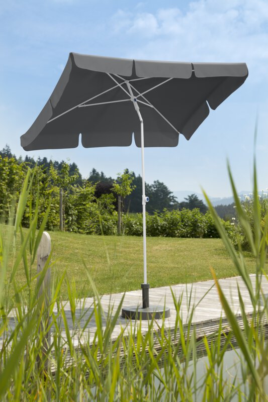 Schneider Ibiza parasol in anthracite, 180x120 cm, on a wooden terrace by a natural swimming pool. Reeds in the foreground, meadow and various green plants in the background.