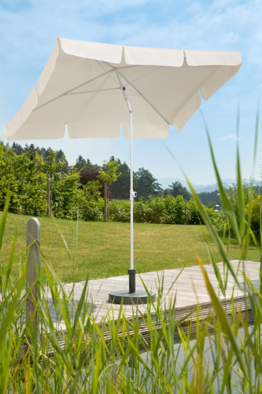 Schneider Ibiza parasol in ecru, 180x120 cm, on a wooden terrace by a natural swimming pool. Reeds in the foreground, meadow and various green plants in the background.