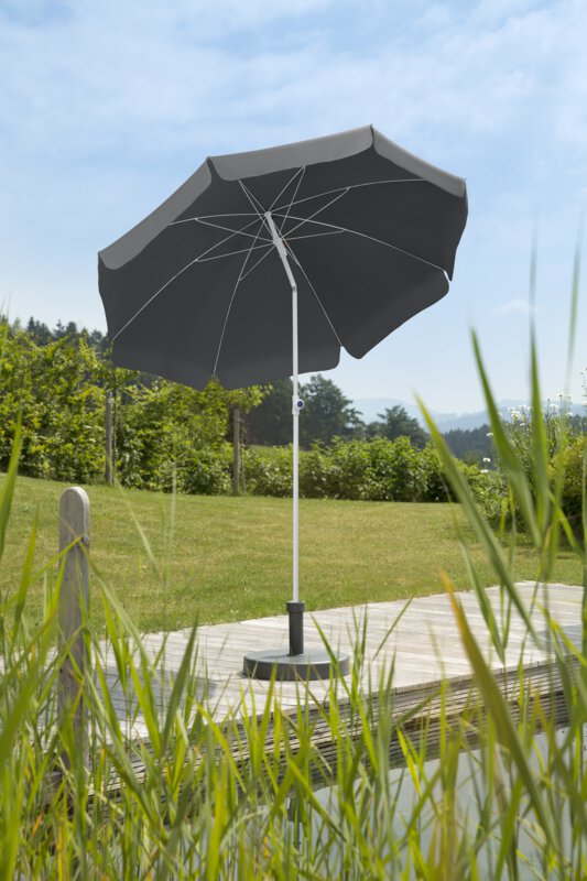 Schneider Ibiza parasol in anthracite, 200 cm in diameter, on a wooden terrace by a natural swimming pool. Reeds in the foreground, meadow and various green plants in the background.