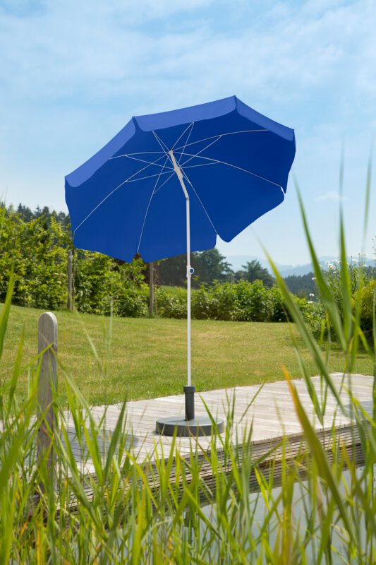Schneider Sonnenschirm Ibiza in Blau, 200 cm Durchmesser, auf einer Holzterrasse an einem Naturpool. Im Vordergrund Schilf, im Hintergrund Wiese und verschiede Grünpflanzen.