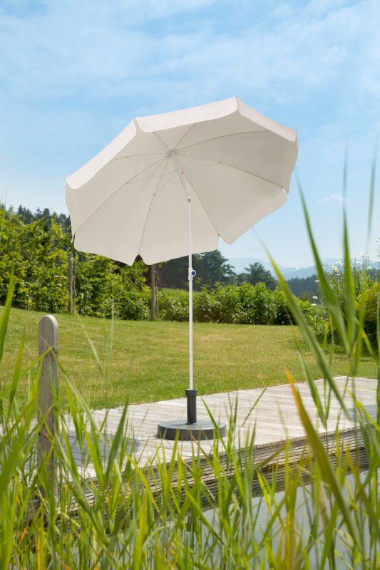 Schneider Ibiza parasol in ecru, 200 cm in diameter, on a wooden terrace by a natural swimming pool. Reeds in the foreground, meadow and various green plants in the background.