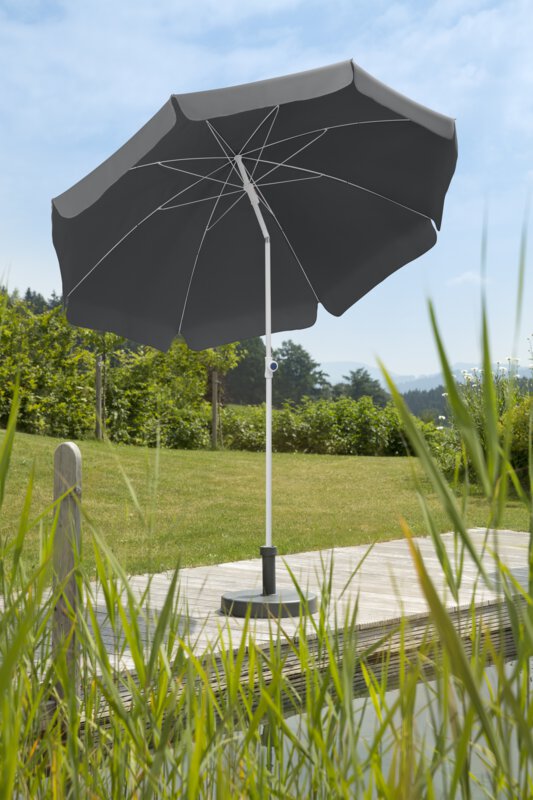 Schneider Ibiza parasol in anthracite, 240 cm in diameter, on a wooden terrace by a natural swimming pool. Reeds in the foreground, meadow and various green plants in the background.
