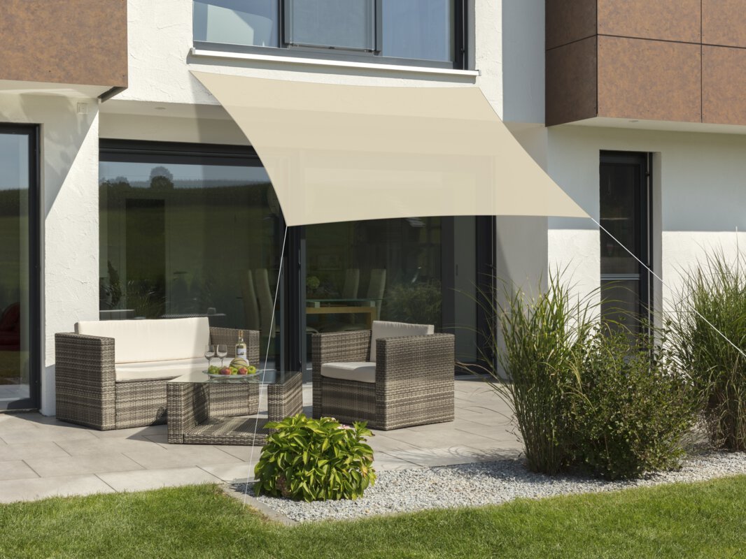 Schneider Sonnensegel Lanzarote in Natur, 300x250 cm, gespannt über eine Terrasse mit Lounge-Möbeln. Auf dem Tisch befindet sich eine Obstschale mit einer Flasche und Gläsern. Im Vordergrund kleine Sträucher und Wiese.