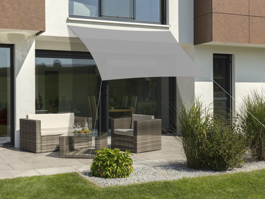 Schneider Sonnensegel Lanzarote in Silbergrau, 300x250 cm, gespannt über eine Terrasse mit Lounge-Möbeln. Auf dem Tisch befindet sich eine Obstschale mit einer Flasche und Gläsern. Im Vordergrund kleine Sträucher und Wiese.