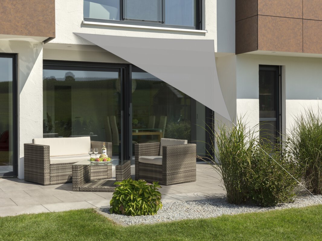 Schneider Sonnensegel Lanzarote in Silbergrau, 360x360x360 cm, gespannt über eine Terrasse mit Lounge-Möbeln. Auf dem Tisch befindet sich eine Obstschale mit einer Flasche und Gläsern. Im Vordergrund kleine Sträucher und Wiese.