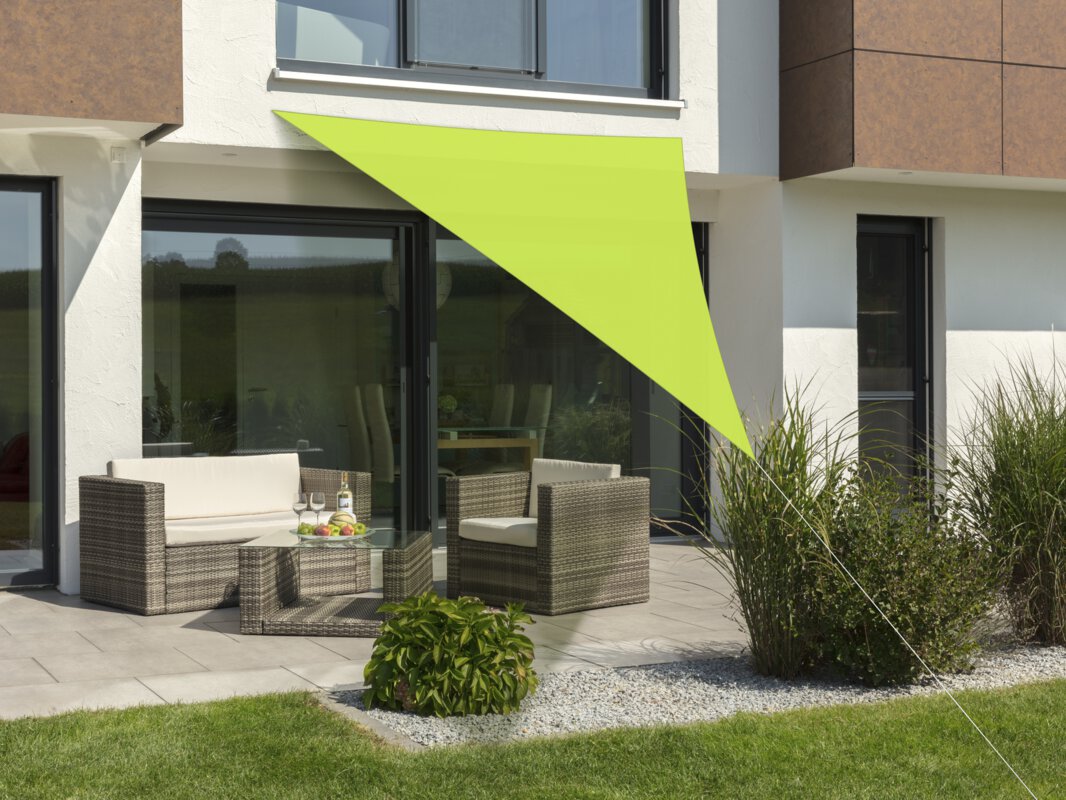 Schneider Sonnensegel Lanzarote in Apfelgrün, 400x400x300 cm, gespannt über eine Terrasse mit Lounge-Möbeln. Auf dem Tisch befindet sich eine Obstschale mit einer Flasche und Gläsern. Im Vordergrund kleine Sträucher und Wiese.