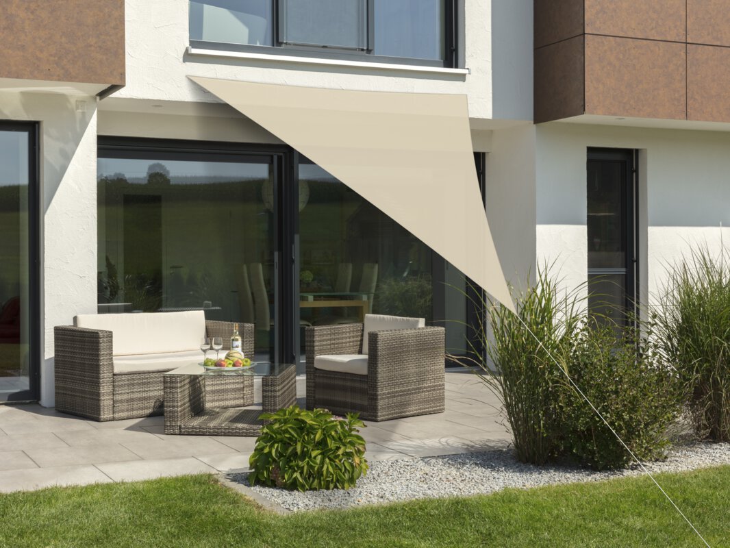 Schneider Sonnensegel Lanzarote in Natur, 400x400x300 cm, gespannt über eine Terrasse mit Lounge-Möbeln. Auf dem Tisch befindet sich eine Obstschale mit einer Flasche und Gläsern. Im Vordergrund kleine Sträucher und Wiese.