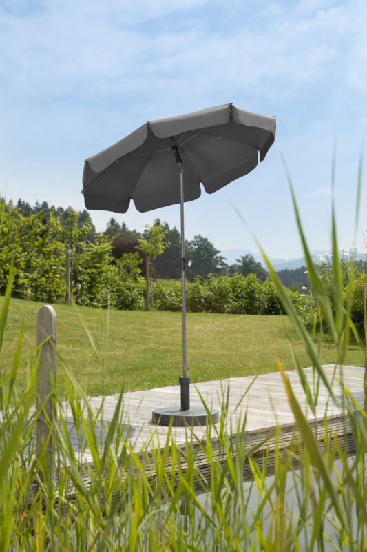 Schneider Locarno parasol in anthracite, 150 cm in diameter, on a wooden terrace by a natural swimming pool. Reeds in the foreground, meadow and various green plants in the background.