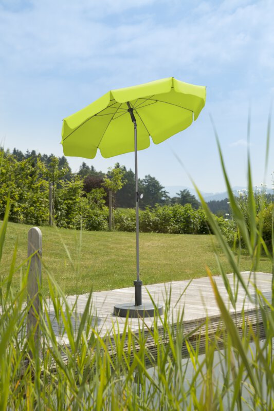 Schneider Locarno parasol in apple green, 150 cm in diameter, on a wooden terrace by a natural swimming pool. Reeds in the foreground, meadow and various green plants in the background.
