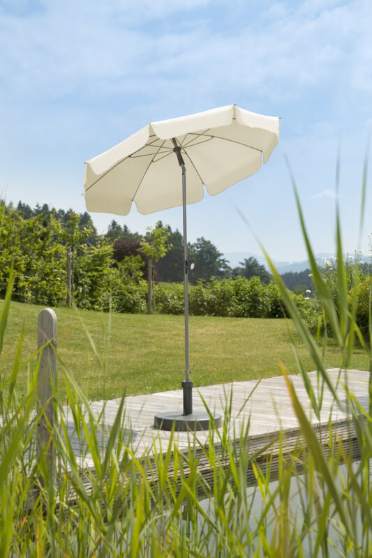 Schneider Locarno parasol in ecru, 150 cm in diameter, on a wooden terrace by a natural swimming pool. Reeds in the foreground, meadow and various green plants in the background.