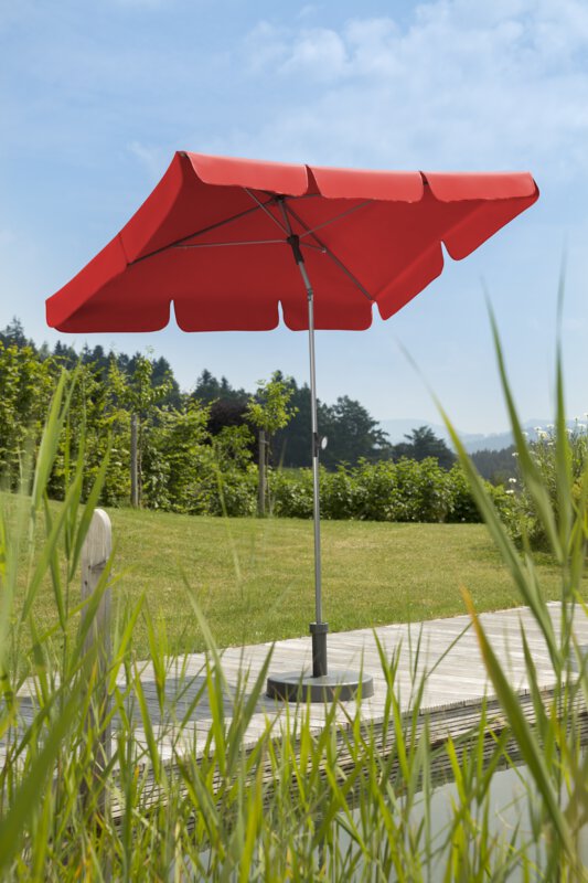 Schneider Locarno parasol in red, 180x120 cm, on a wooden terrace by a natural swimming pool. Reeds in the foreground, meadow and various green plants in the background.
