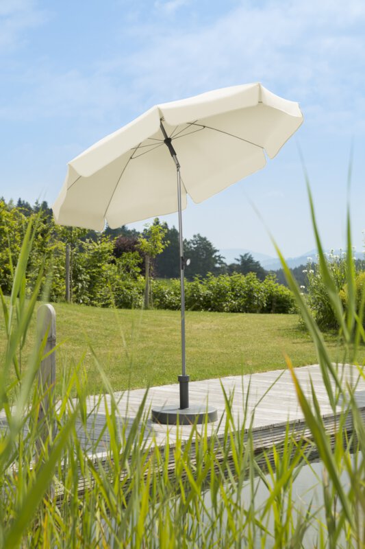 Schneider Locarno parasol in ecru, 200 cm in diameter, on a wooden terrace by a natural swimming pool. Reeds in the foreground, meadow and various green plants in the background.