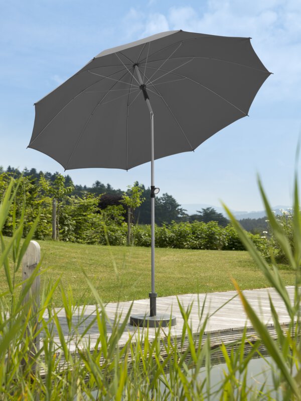 Schneider parasol Locarno in anthracite, 220 cm in diameter, on a wooden terrace by a natural swimming pool. Reeds in the foreground, meadow and various green plants in the background.