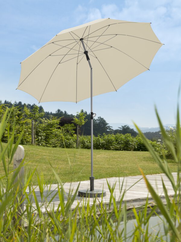 Schneider parasol Locarno in ecru, 220 cm in diameter, on a wooden terrace by a natural swimming pool. Reeds in the foreground, meadow and various green plants in the background.