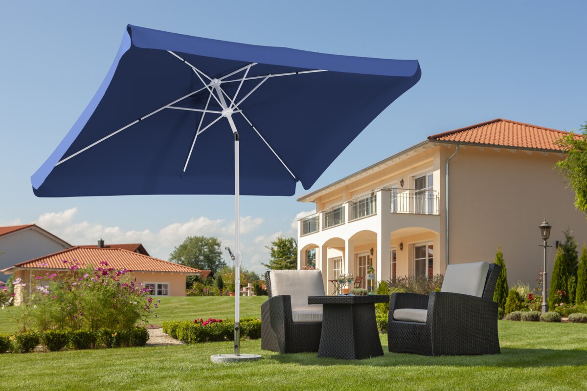 Schneider Oslo parasol in blue, 200x300 cm, on a lawn above lounge furniture. In the background blooming flowers, shrubs and houses in Mediterranean style.