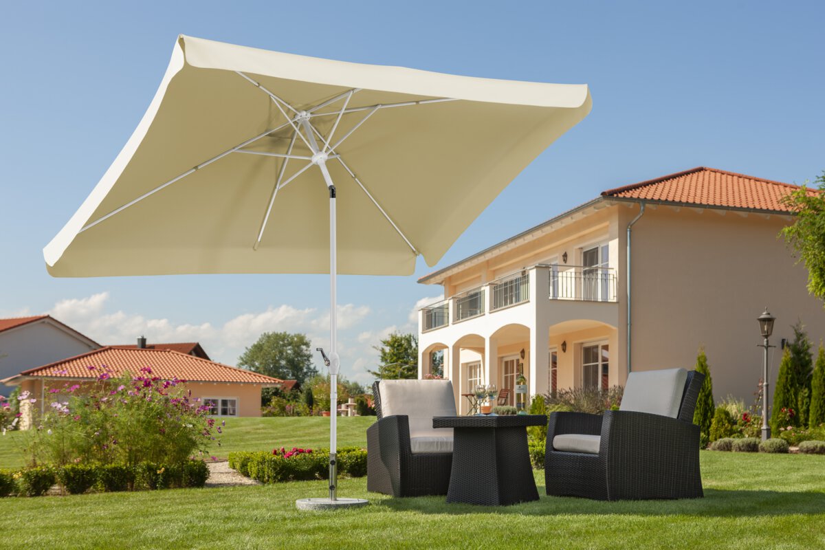 Schneider Sonnenschirm Oslo in Natur, 200x300 cm, auf einer Wiese über Lounge-Möbeln. Im Hintergrund blühende Blumen, Sträucher und Häuser im mediterranen Stil.
