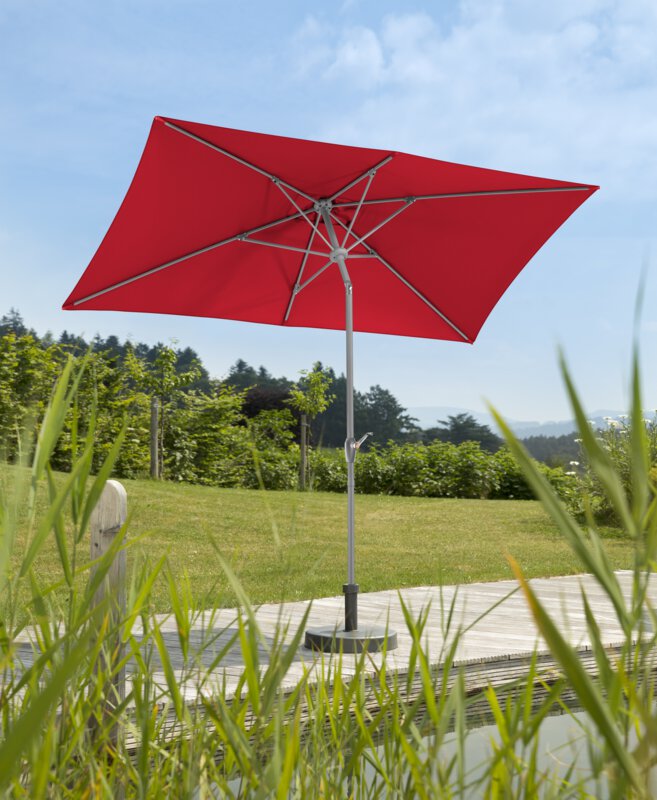 Schneider Porto parasol in red, 300x200 cm, on a wooden terrace by a natural swimming pool. Reeds in the foreground, meadow and various green plants in the background.