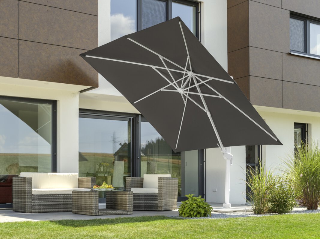 Schneider parasol Rhodos Twist Bianco in anthracite, 300x300 cm, inclined, on a terrace with lounge furniture. A fruit bowl sits on the table. Small shrubs and a meadow are in the foreground.