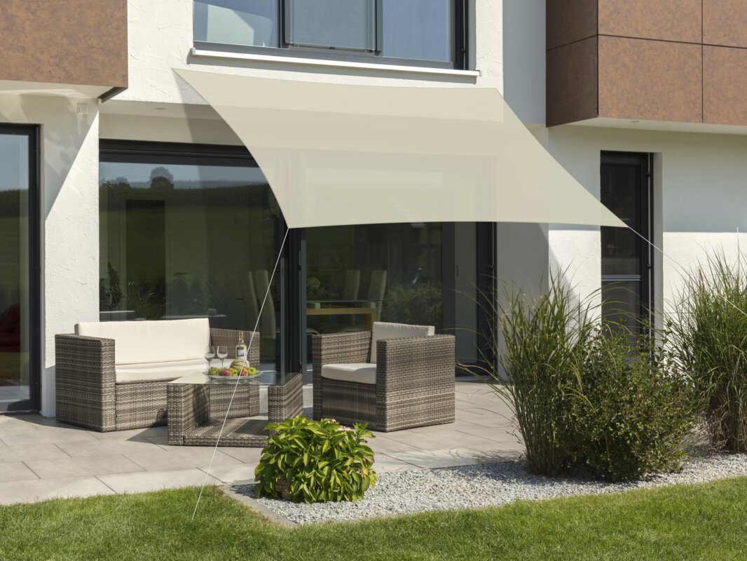 Schneider Sonnensegel Teneriffa in Natur, 360x250 cm, gespannt über eine Terrasse mit Lounge-Möbeln. Auf dem Tisch befindet sich eine Obstschale mit einer Flasche und Gläsern. Im Vordergrund kleine Sträucher und Wiese.