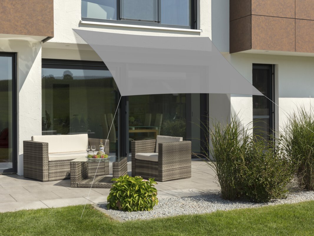 Schneider Sonnensegel Teneriffa in Silbergrau, 360x250 cm, gespannt über eine Terrasse mit Lounge-Möbeln. Auf dem Tisch befindet sich eine Obstschale mit einer Flasche und Gläsern. Im Vordergrund kleine Sträucher und Wiese.