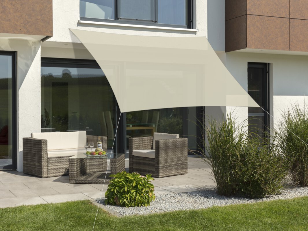 Schneider Sonnensegel Teneriffa in Natur, 360x360 cm, gespannt über eine Terrasse mit Lounge-Möbeln. Auf dem Tisch befindet sich eine Obstschale mit einer Flasche und Gläsern. Im Vordergrund kleine Sträucher und Wiese.