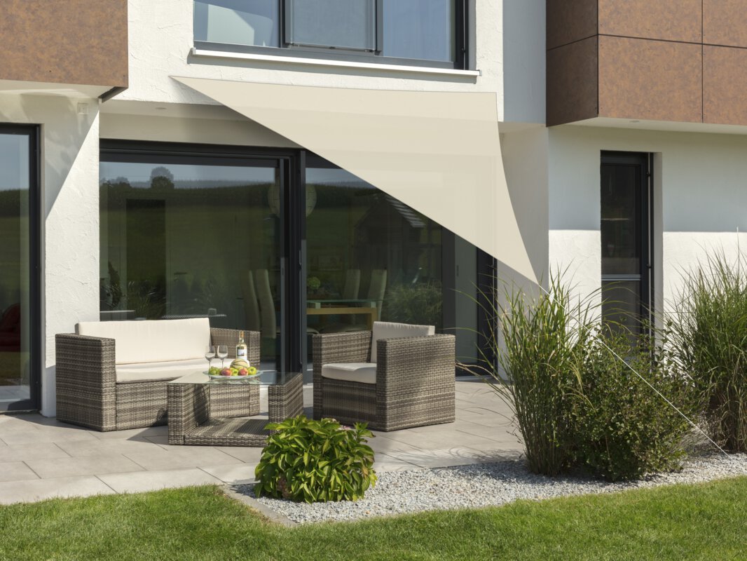 Schneider Sonnensegel Teneriffa in Natur, 360x360x360 cm, gespannt über eine Terrasse mit Lounge-Möbeln. Auf dem Tisch befindet sich eine Obstschale mit einer Flasche und Gläsern. Im Vordergrund kleine Sträucher und Wiese.