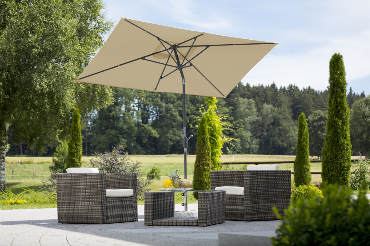 Schneider's Tunis parasol in ecru, 270x150 cm, on a terrace with lounge furniture. A fruit bowl sits on the table. In the background are shrubs, a fence, a meadow with trees and a forest.