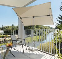 Schneider Sonnenschirm Novara 190x140 cm in Natur auf einer Terrasse mit Stuhl und Beistelltisch. Im Hintergrund Bäume und ein Flusslauf. Der Schirm bietet hohen UV-Schutz und ist in alle Richtungen dreh- und schwenkbar, seitlich verschiebbar und höhenverstellbar.
