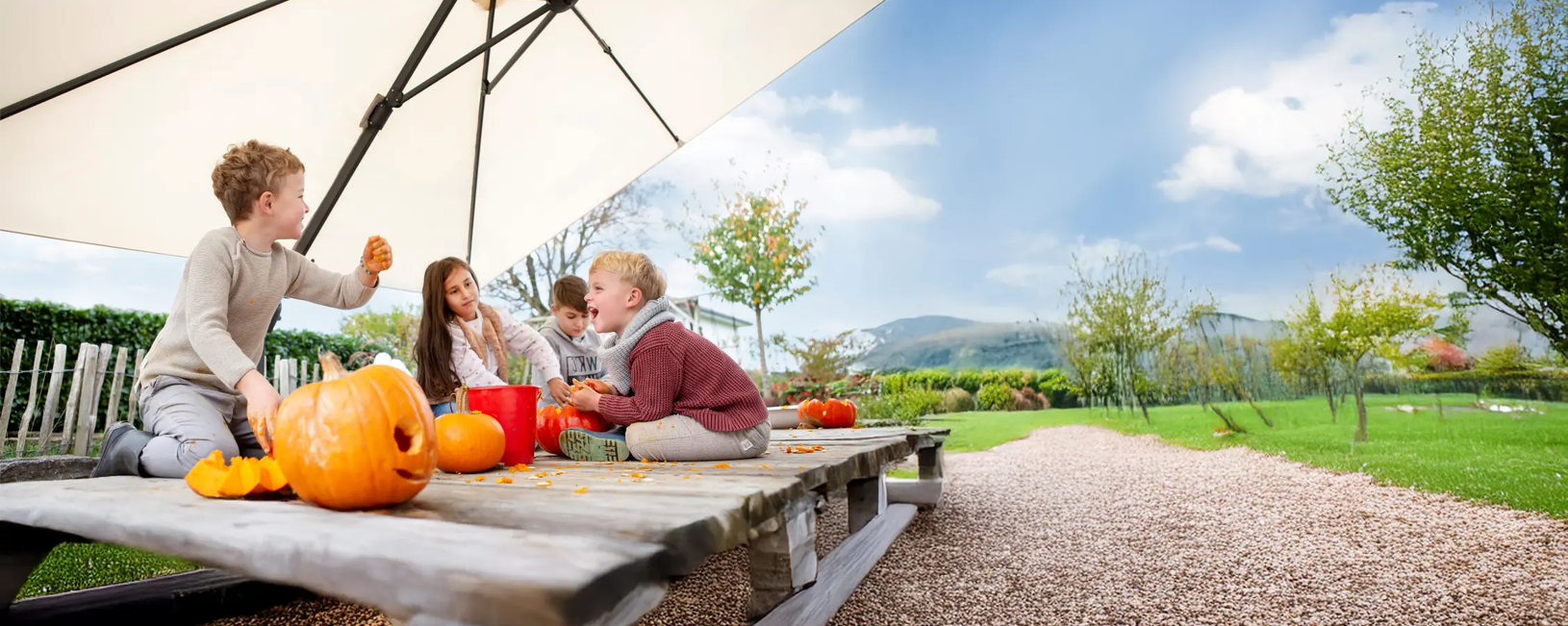 Schneider cantilever parasol Rhodos Twist in action during pumpkin carving– three-dimensionally adjustable for flexible sun protection in the garden and on the terrace. Four children are sitting under the Rhodos Twist cantilever parasol carving pumpkins. Thanks to its three-dimensional adjustability, the parasol provides optimal UV protection – ideal for garden and terrace.